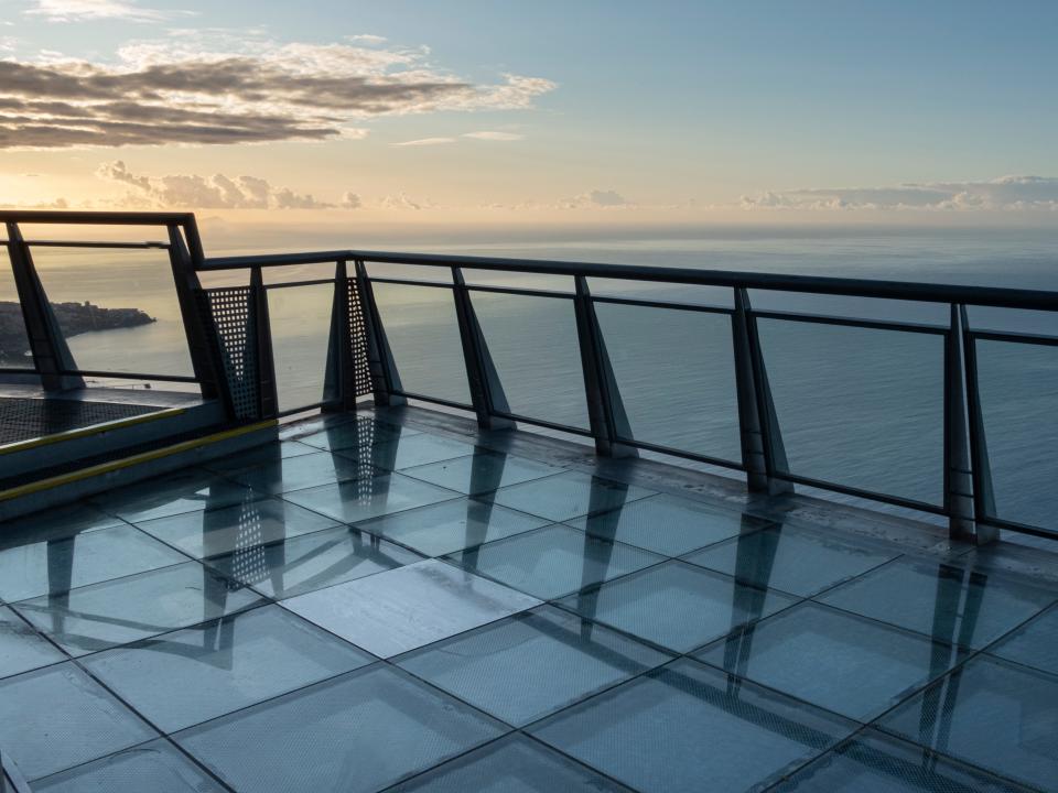 A lookout over the ocean, with glass tiles as flooring, at sunset.