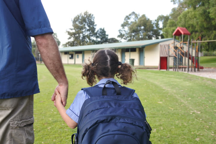 A man holds his daughter's hand while walking her to school.