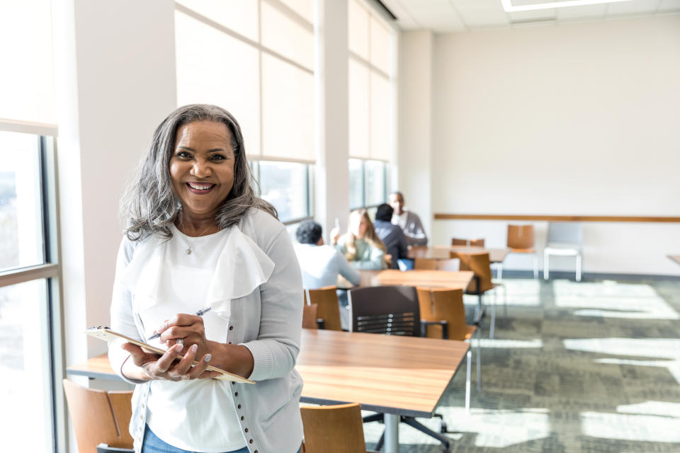 a smiling woman with a clipboard in a college classroom