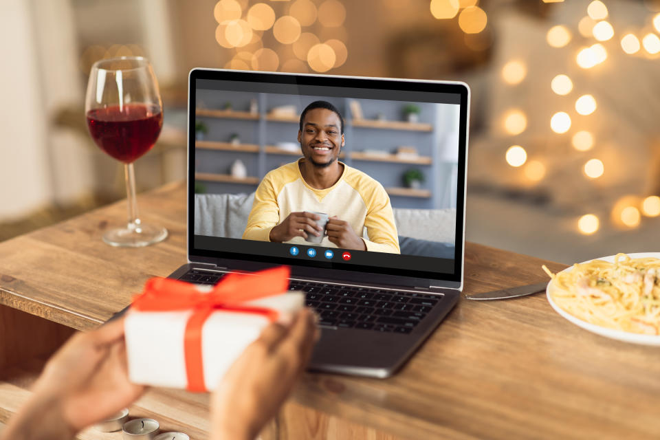 Virtual celebration during covid pandemic. Young black woman having online date with her boyfriend or husband, showing wrapped gift box at laptop screen, having wine at home