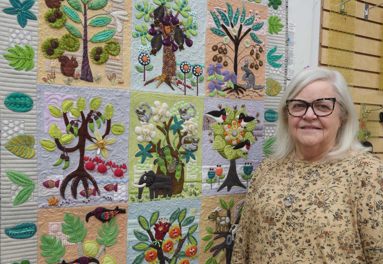 Sue Spargo with her folk art quilt “Forest for the Trees,” featuring trees and animals from all over the world, at her store in Green.