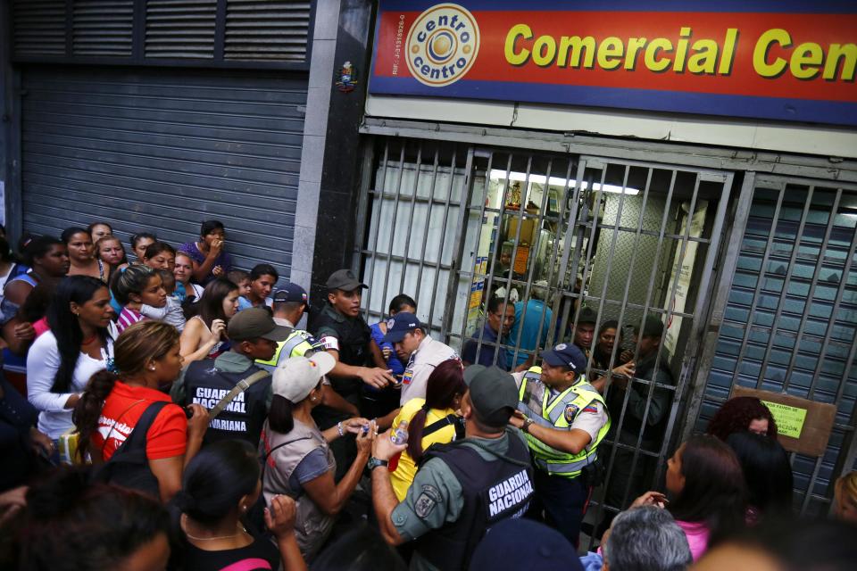 People line up to buy toilet paper and baby diapers as national guards control the access at a supermarket in downtown Caracas January 19, 2015. There's a booming new profession in Venezuela: standing in line. The job usually involves starting before dawn, enduring long hours under the Caribbean sun, dodging or bribing police, and then selling a coveted spot at the front of huge shopping lines. As Venezuela's ailing economy spawns unprecedented shortages of basic goods, panic-buying and a rush to snap up subsidized food, demand is high and the pay is reasonable. Picture taken January 19, 2015. REUTERS/Jorge Silva (VENEZUELA - Tags: POLITICS BUSINESS SOCIETY)