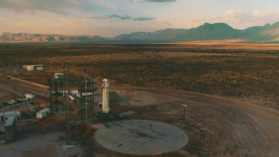 A white and blue rocket stands on its launch pad awaiting liftoff in the Texas desert