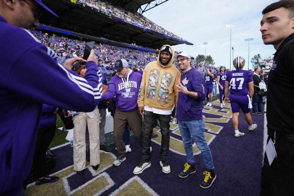 Former Washington quarterback Michael Penix Jr., in gold, takes photos with fans before an NCAA college football game against Michigan, Saturday, Oct. 5, 2024, in Seattle. (AP Photo/Lindsey Wasson)