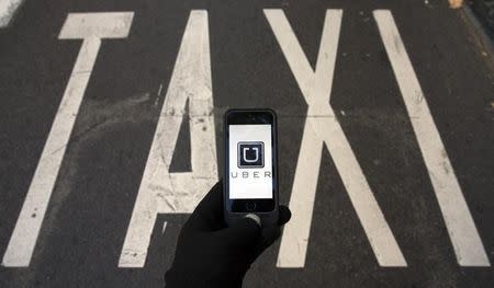 The logo of car-sharing service app Uber on a smartphone over a reserved lane for taxis in a street is seen in this photo illustration taken in Madrid on December 10, 2014. REUTERS/Sergio Perez