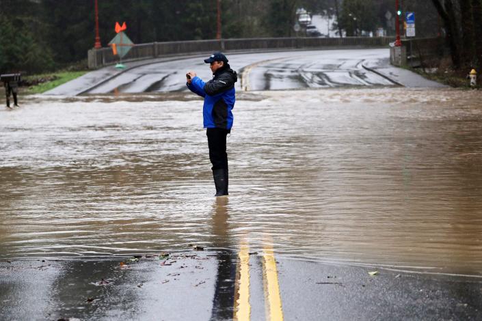 A man stands in a roadway flooded by Issaquah Creek and takes photos Thursday, Feb. 6, 2020, in Issaquah, Wash. Heavy rain sent the creek over a major roadway, under an apartment building east of Seattle and up to the foundations of homes as heavy rains pounded the region. A flood watch was in effect through Friday afternoon across most of western Washington.