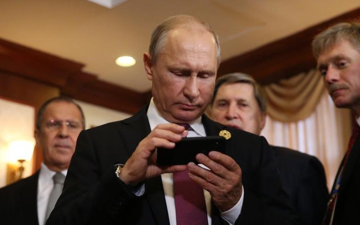 Der russische Präsident Vladimir Putin (C) hält ein iPhone, während sein Sprecher Dmitry Peskov (R) vor einem bilateralen Treffen mit dem philippinischen Präsidenten Rodrigo Duterte zuschaut