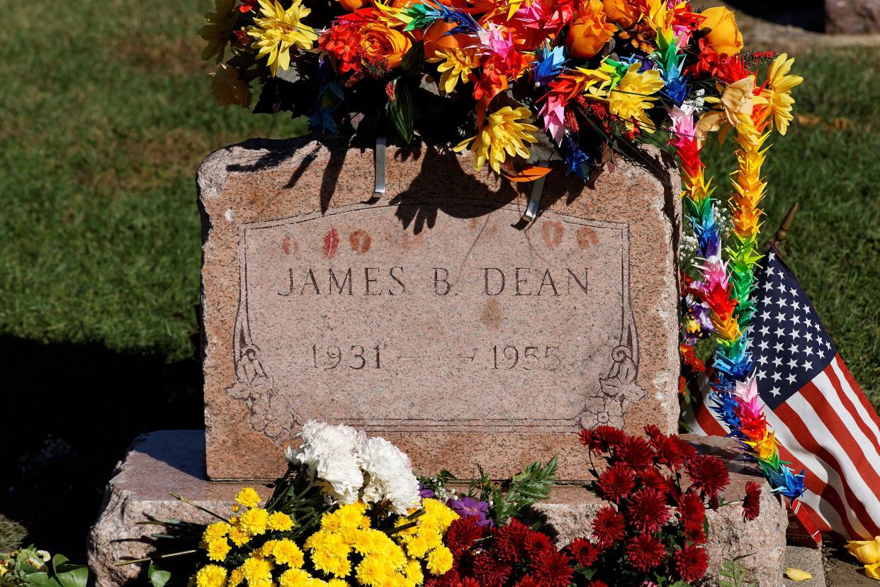 James Dean's grave in the Park Cemetery, Fairmount, Indiana, kiss marks on the headstone, surrounded by several brightly colored flower bouquets and an American flag with grass in the background