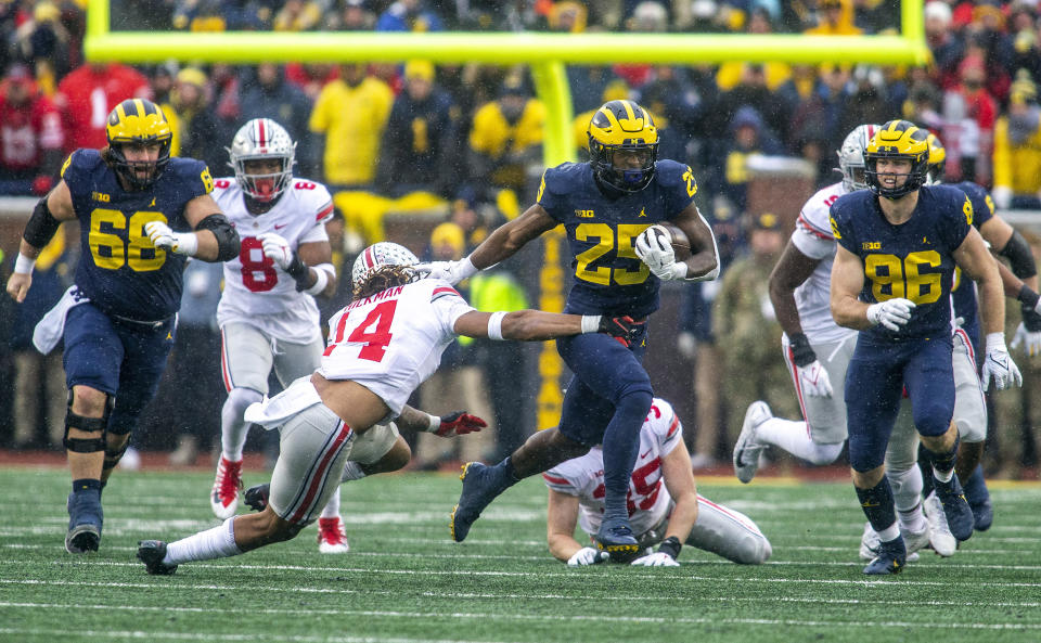 FILE - Michigan running back Hassan Haskins (25) breaks a tackle from Ohio State safety Ronnie Hickman (14) in the fourth quarter of an NCAA college football game in Ann Arbor, Mich., Saturday, Nov. 27, 2021. Michigan won 42-27. (AP Photo/Tony Ding, File)