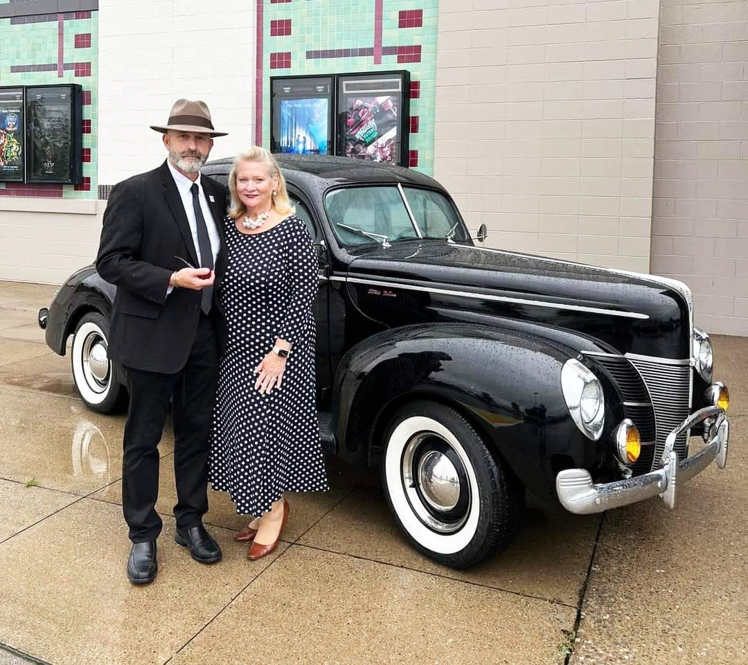 Oak Ridge Mayor Pro Tem Jim Dodson and his wife, Becky, don attire reminiscent of the 1940s for the premiere of "Oppenheimer" in Oak Ridge. They are posing outside a vintage car outside the movie theater.