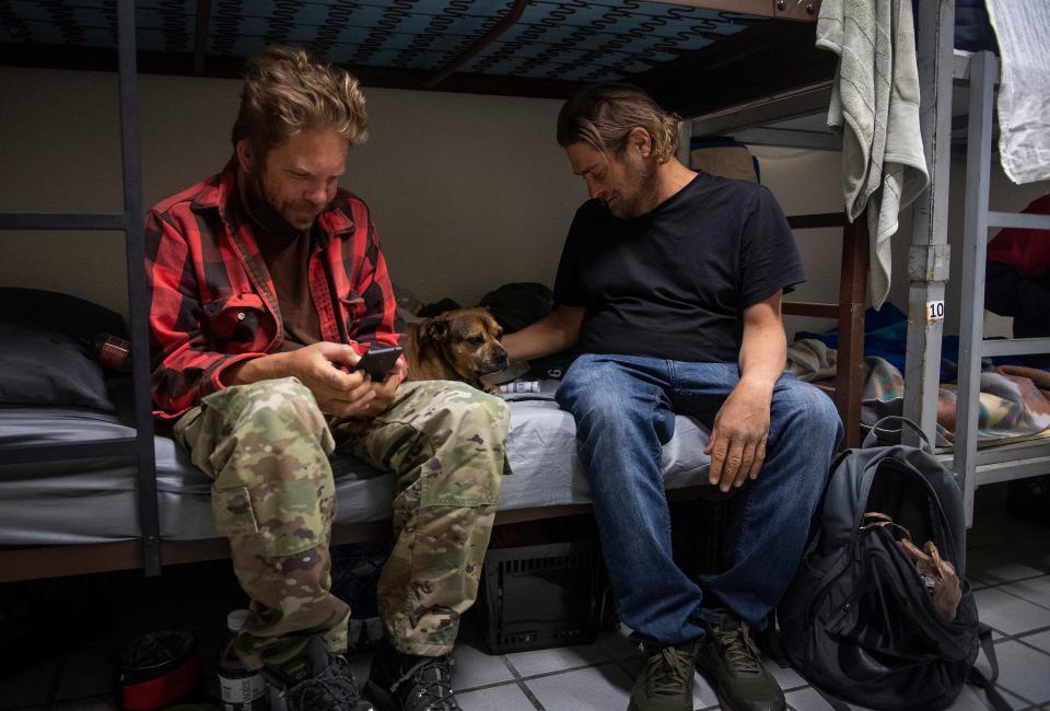 Das Lowrie, left, checks his phone as John Carlin pets Lowrie's dog, Brando, at the Fort Collins Rescue Mission in Fort Collins last year.