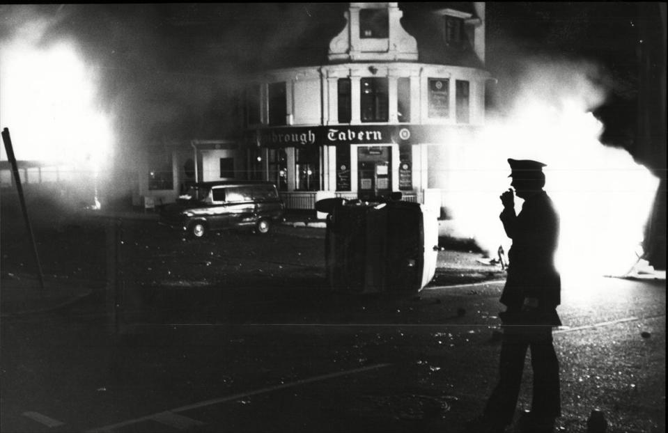 Southall Riot 1981 - A Lone Policeman Radios For Help Beside His Overturned Van Outside The Blazing Hambrough Tavern. (Paul Fievez/ANL/Shutterstock)