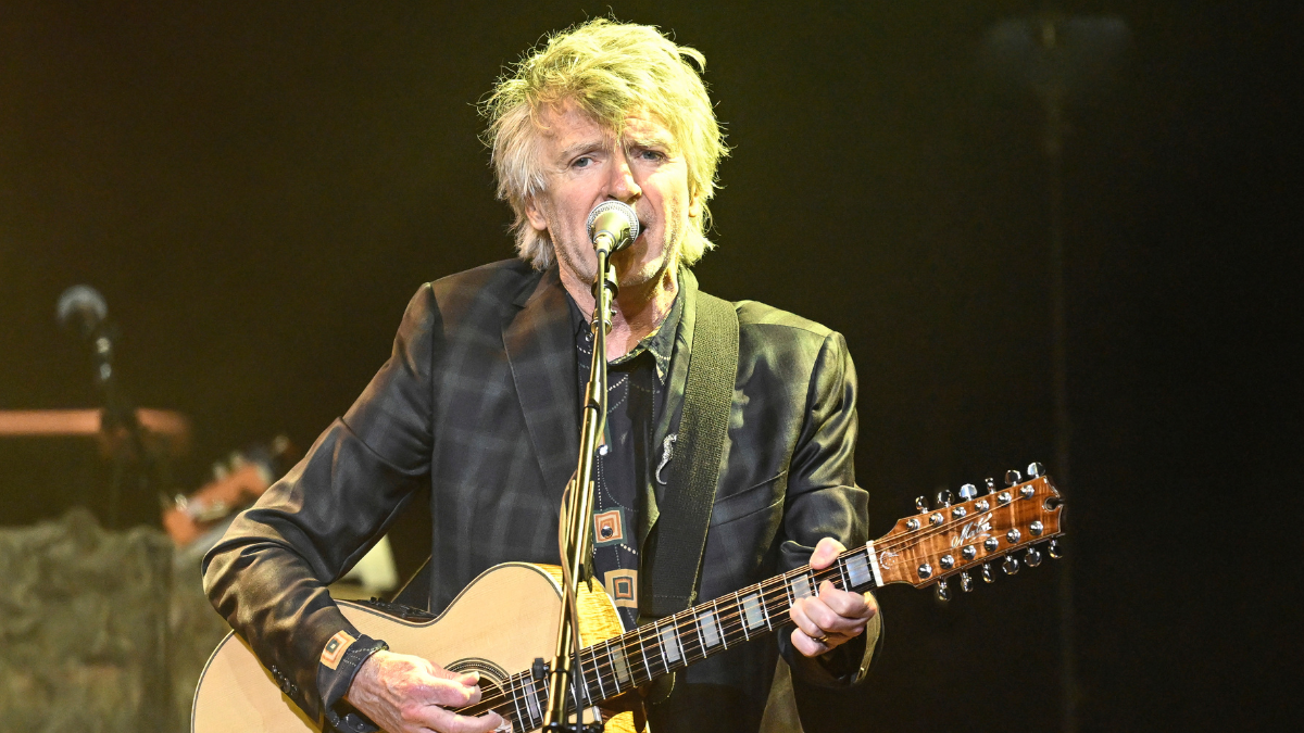  Neil Finn playing an acoustic guitar on stage. 