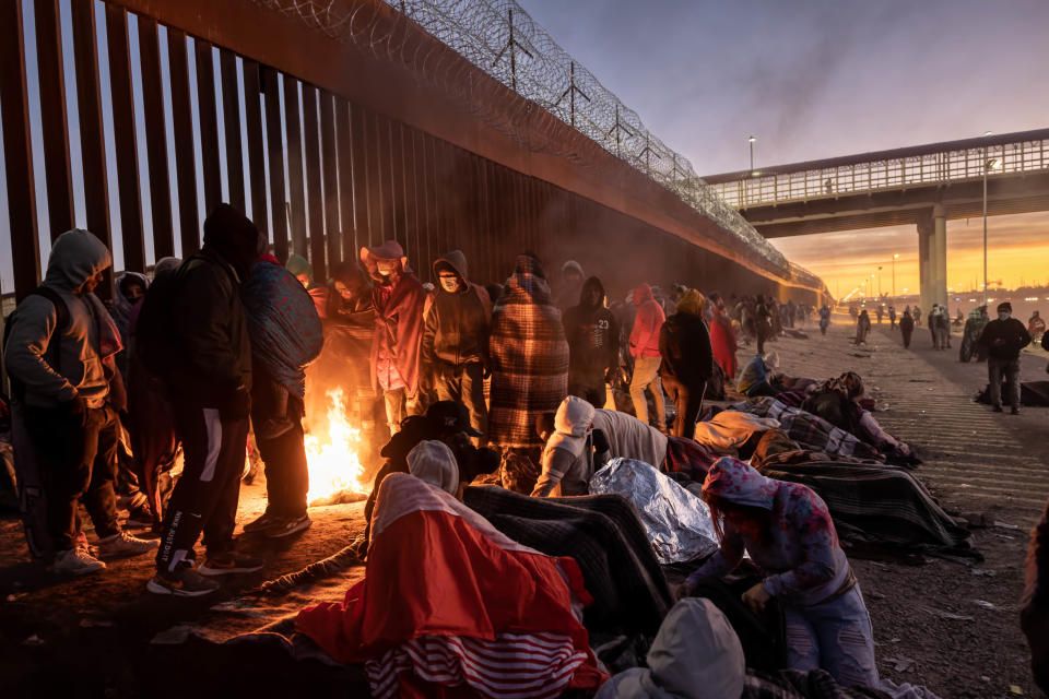 Immigrants keep warm by a fire at dawn after spending the night outside next to the U.S.-Mexico border fence on Dec. 22, 2022, in El Paso, Texas.  / Credit: Getty Images