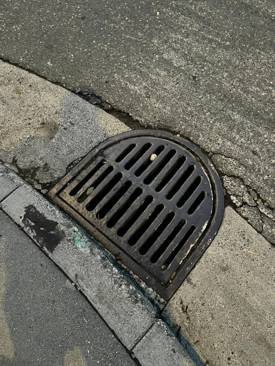 Storm drain grate with a golf ball lodged in the slot