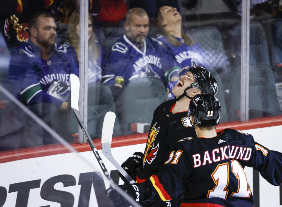 Vancouver Canucks fans, top, look on as Calgary Flames forward Jonathan Huberdeau, center, celebrates after his goal with teammate forward Mikael Backlund (11) during third-period NHL hockey game action in Calgary, Alberta, Thursday, Nov. 16, 2023. (Jeff McIntosh/The Canadian Press via AP)