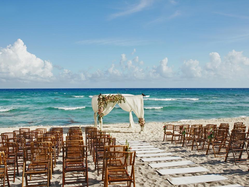 Chairs lined up on sand with alter in front of ocean and blue sky in background
