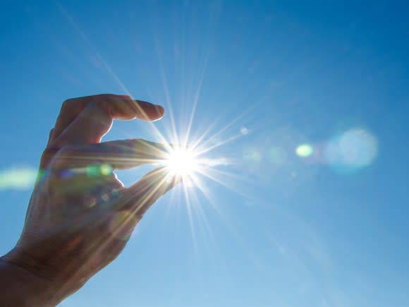 Fingers appearing to pinch the sun in the sky