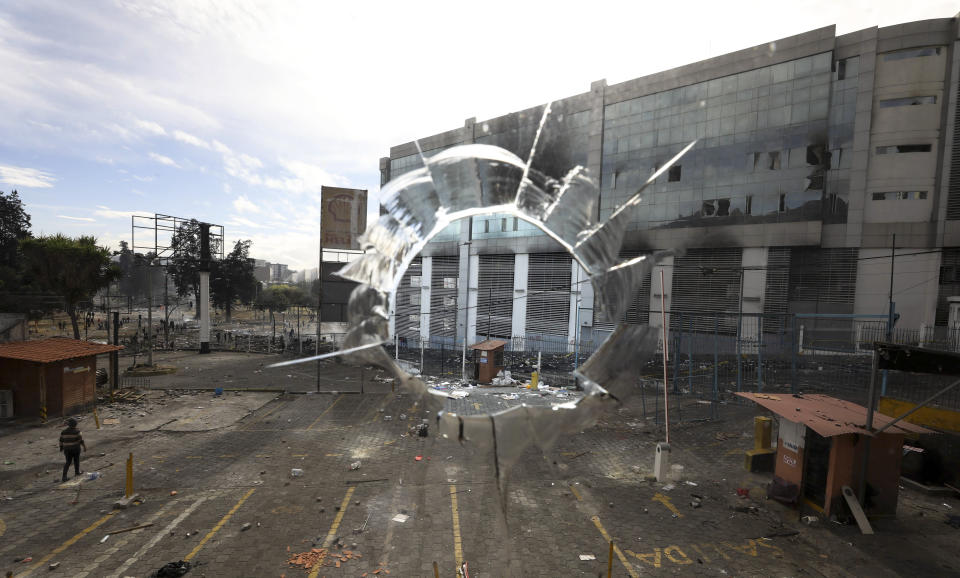 Photographed through a broken window, the national auditor's office stands across the street, damaged after it was attacked by anti-government protesters in Quito, Ecuador, Sunday, Oct. 13, 2019. Ecuador's army patrolled the streets of the capital Sunday as the government of President Lenín Moreno and indigenous leaders prepared for talks to end more than a week of fuel price protests that have led to attacks on government buildings and media offices, and prompted a 24-hour curfew. (AP Photo/Fernando Vergara)