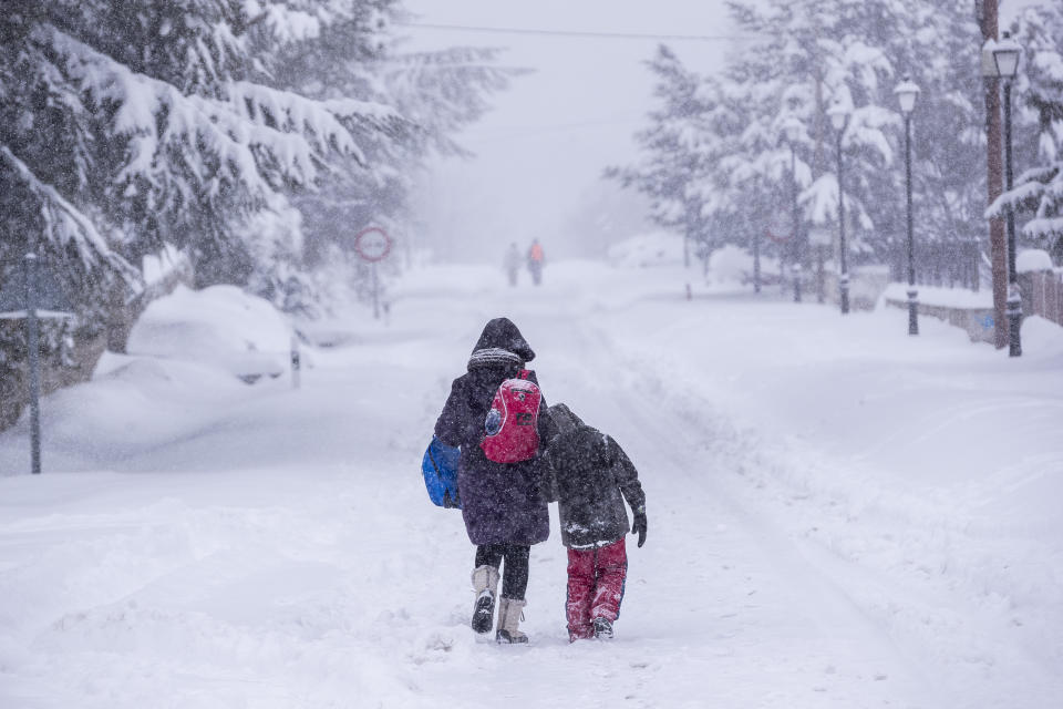 People walk under a heavy snowfall in Bustarviejo, outskirts of Madrid, Spain, Saturday, Jan. 9, 2021. A persistent blizzard has blanketed large parts of Spain with 50-year record levels of snow, halting traffic and leaving thousands trapped in cars or in train stations and airports that suspended all services as the snow kept falling on Saturday. Half of Spain is on alert, with five provinces on their highest level of warning. (AP Photo/Bernat Armangue)