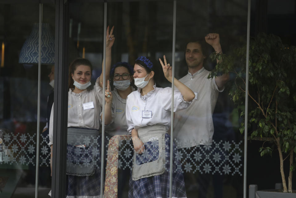 Staff in a restaurant gesture in support as participants take part in an opposition rally protesting the official presidential election results in Minsk, Belarus, Sunday, Sept. 27, 2020. Tens of thousands of demonstrators marched in the Belarusian capital calling for the authoritarian president's ouster, some wearing cardboard crowns to ridicule him, on Sunday as the protests that have rocked the country marked their 50th consecutive day. (AP Photo/TUT.by)