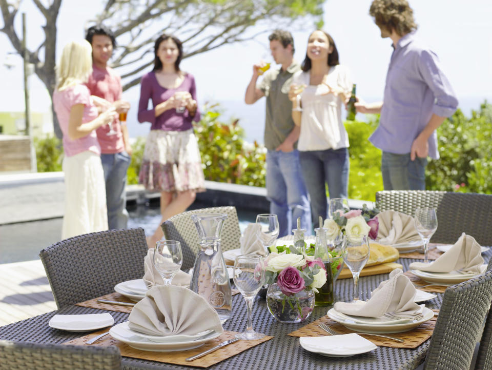 Friends standing outside a home drinking near a set table.