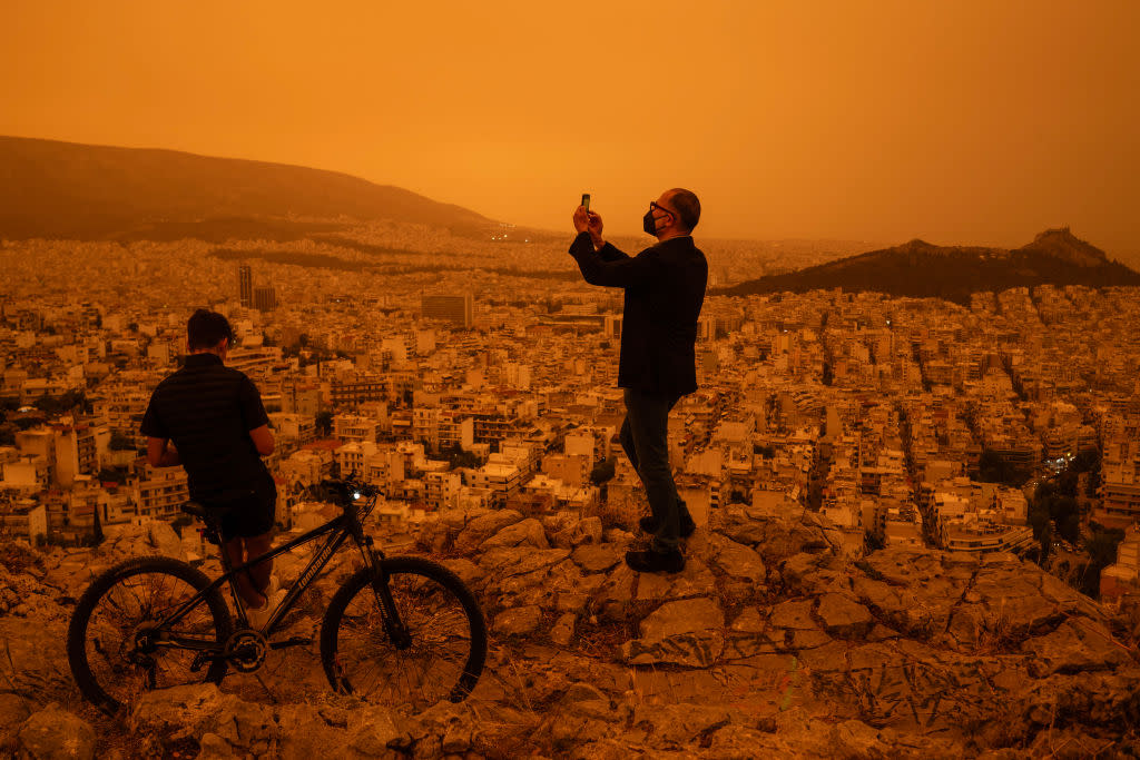 A man takes a photograph of the city of Athens from the Tourkovounia hills, as southerly winds carry waves of Saharan dust to the city.<span class="copyright">Angelos Tzortzinis—Getty Images</span>