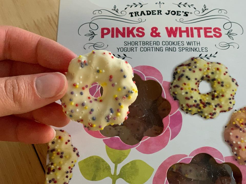 hand holding trader joe's pink and white cookies in front of white box