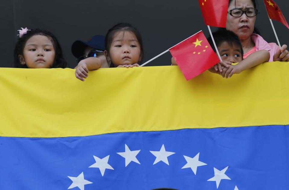 Chinese children holding a Chinese flag and standing over a Venezuela's flag watch the navy hospital ship "The Peace Ark" arriving at the port in La Guaira, Venezuela, Saturday, Sept. 22, 2018. The stop by the People's Liberation Army Navy's ship is the latest in an 11-nation "Mission Harmony" tour and will provide free medical treatment for Venezuelans. (AP Photo/Ariana Cubillos)