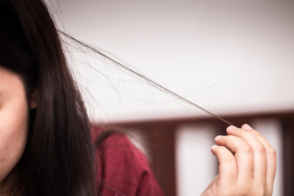 A female, whose face is only partially pictured, pulls on a long strand of her long brown hair. People with trichotillomania have a compulsion to pull out hair from their scalp, eyebrows or other areas of the body. 