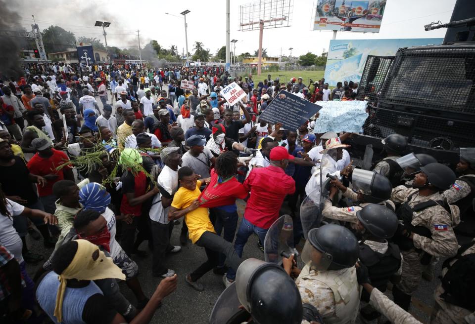 Police in riot gear scuffle with protesters on the edge of a large group