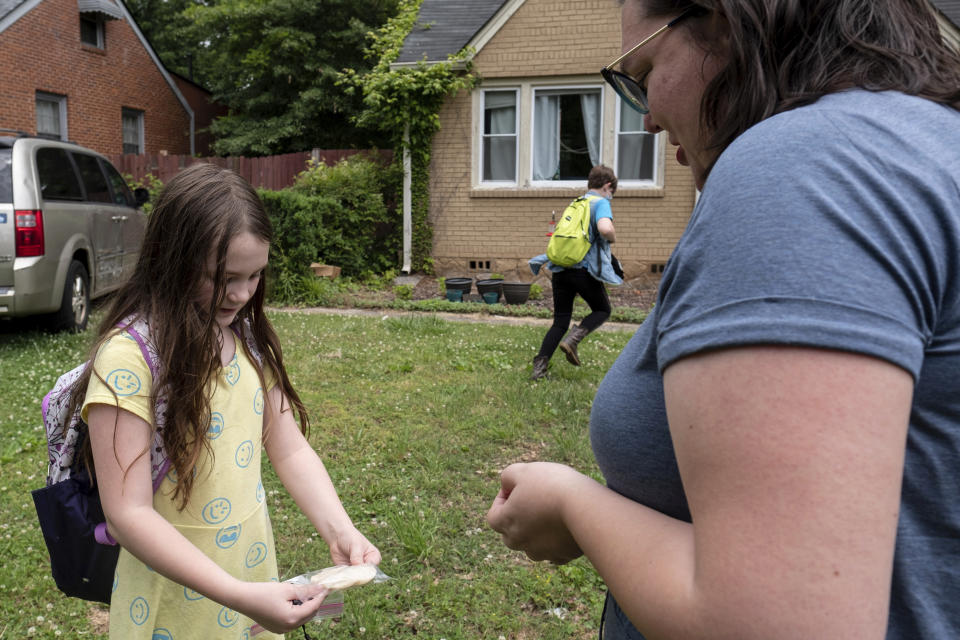 Abby Norman, right, looks at a project made by her daughter Priscilla, 9, left, as Juliet, 11, runs inside as they arrive home from school to the family's home in Decatur, Ga., Tuesday, May 18, 2021. Priscilla was in tears the first morning of school testing this year because she felt pressure to do well, but didn't feel prepared after remote learning. (AP Photo/Ben Gray)