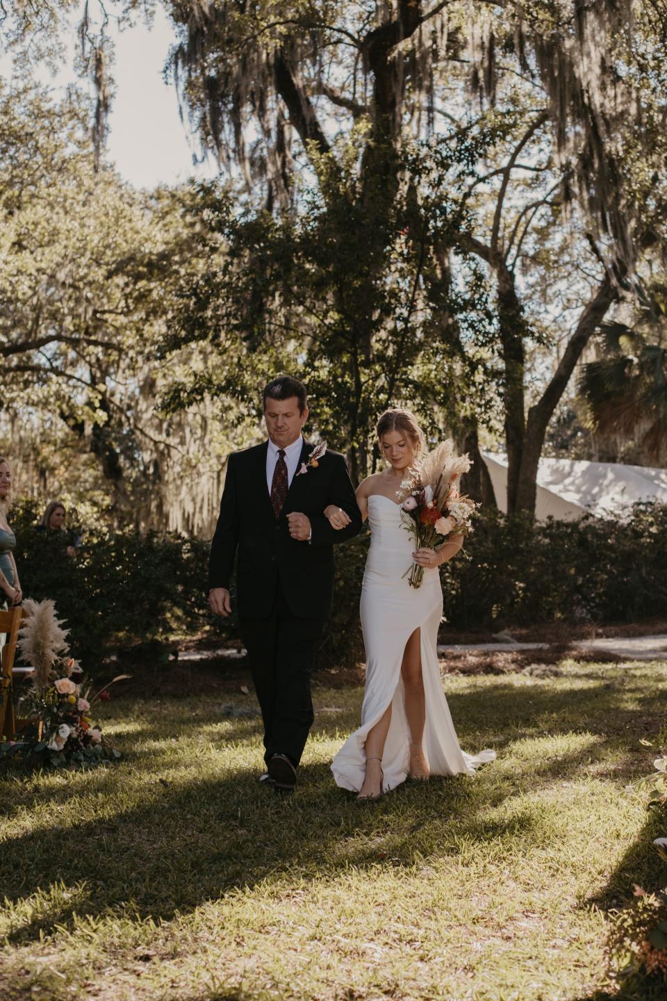 A bride walks down a grass aisle on her wedding day with her father.