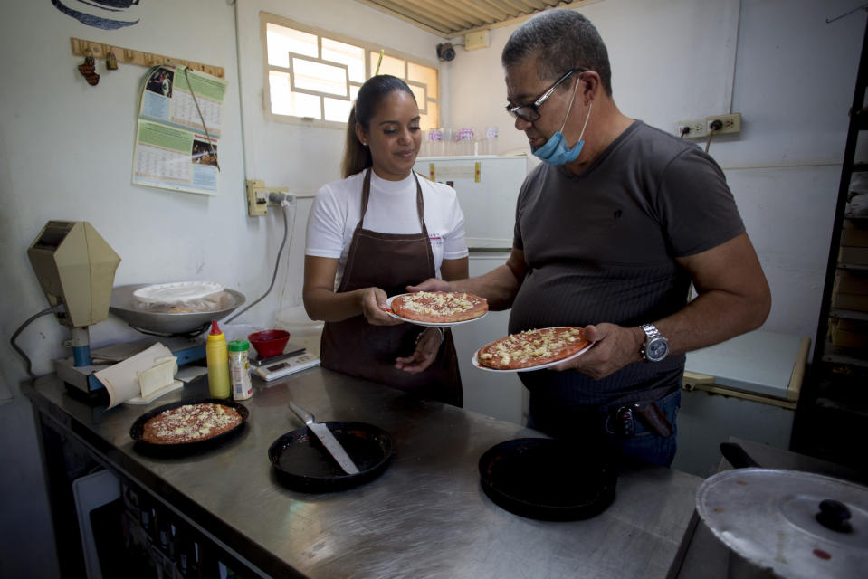 Natalhie Fonseca ayuda a su esposo Ernesto Collazo a preparar pizzas que él vende desde su casa en La Habana, Cuba, el domingo 26 de diciembre de 2021. (AP Foto/Ismael Francisco)