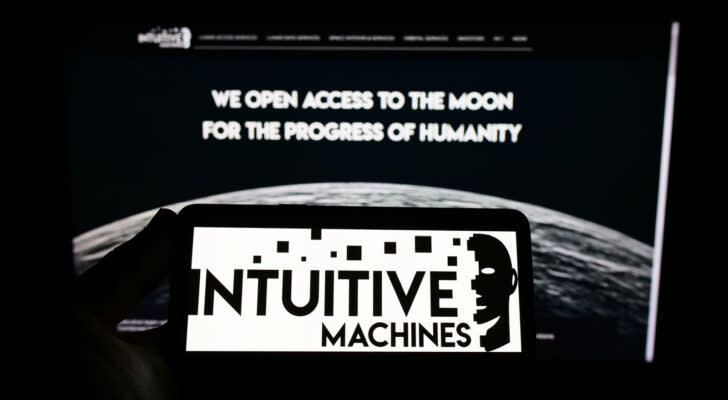 Intuitive Machines (LUNR) black and white logo displayed on smartphone screen with desktop screen behind it showing company website and image of moon
