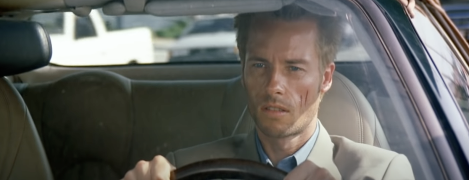 A man sits in the drivers seat of a car, gripping the wheel