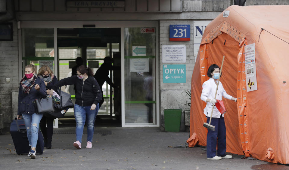 People leaving a hospital pass by a tent put up before the entrance for testing all those entering for COVID-19 in Warsaw, Poland, on Tuesday, Oct. 20, 2020. Poland is seeing a sharp spike in new cases daily of coronavirus infections, filling up hospital beds. Poland's government is transforming the National Stadium in Warsaw into a field hospital to handle the surging number of people infected with the coronavirus, and expects it to be operational within days, officials said. (AP Photo/Czarek Sokolowski)