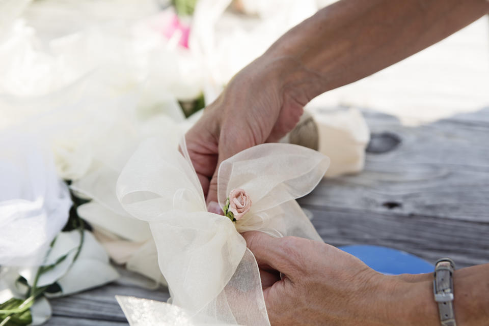 Woman’s hands making DIY wedding decorations by the beach on a sunny day. She is making a knot with tulle and fabric flower. No face. Horizontal close up outdoors shot with copy space.