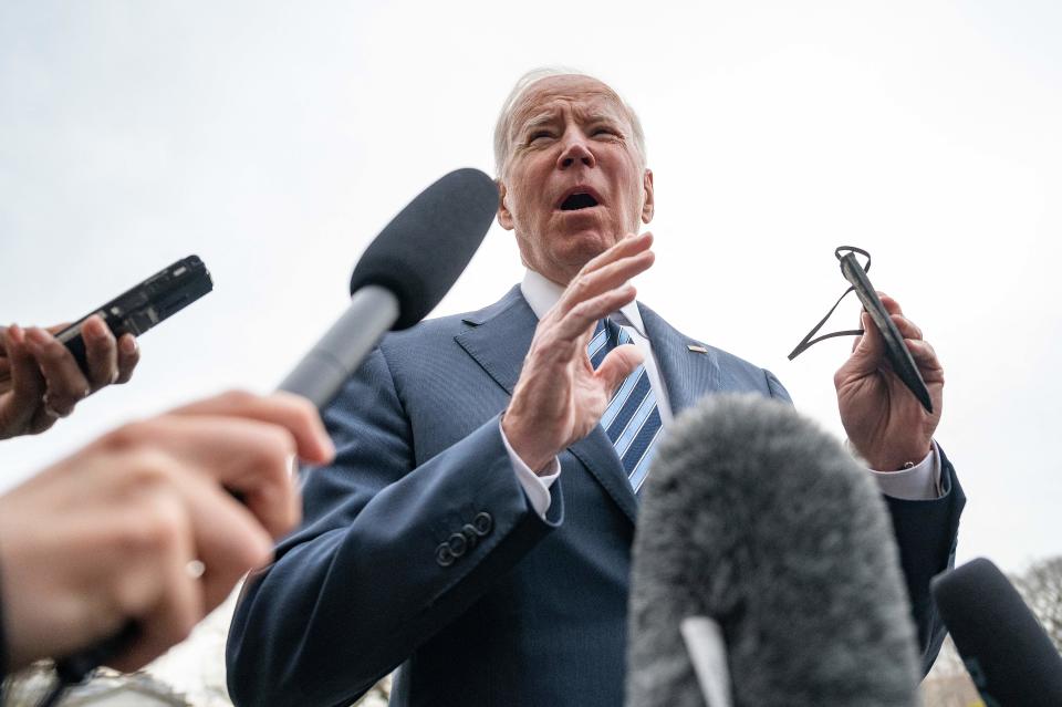 President Biden surrounded by journalists holding microphones. 