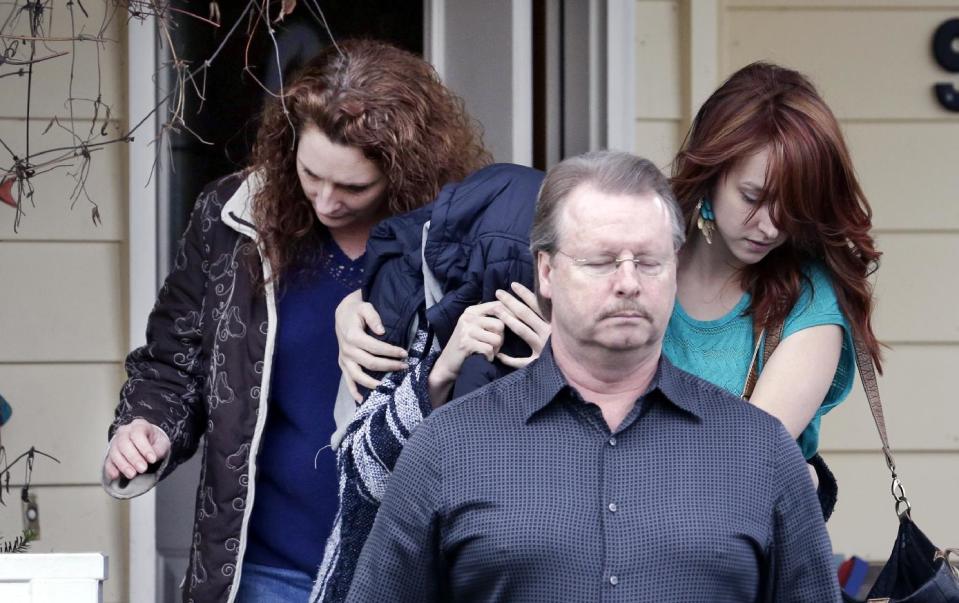 ADDS STATEMENT FROM KNOX SPOKESMAN DAVID MARRIOTT-An unidentified woman, center, is hidden under a jacket while being escorted from the home of Amanda Knox's mother, Thursday, Jan. 30, 2014, in Seattle. Knox’s family spokesman, David Marriott, said Thursday that Knox was at the house when an Italian court upholding her murder conviction was read Thursday, but said he didn’t know whether the person who emerged was Knox. On Friday, Marriott stated he had made inquiries and that the person under the jacket wasn’t Knox. (AP Photo)