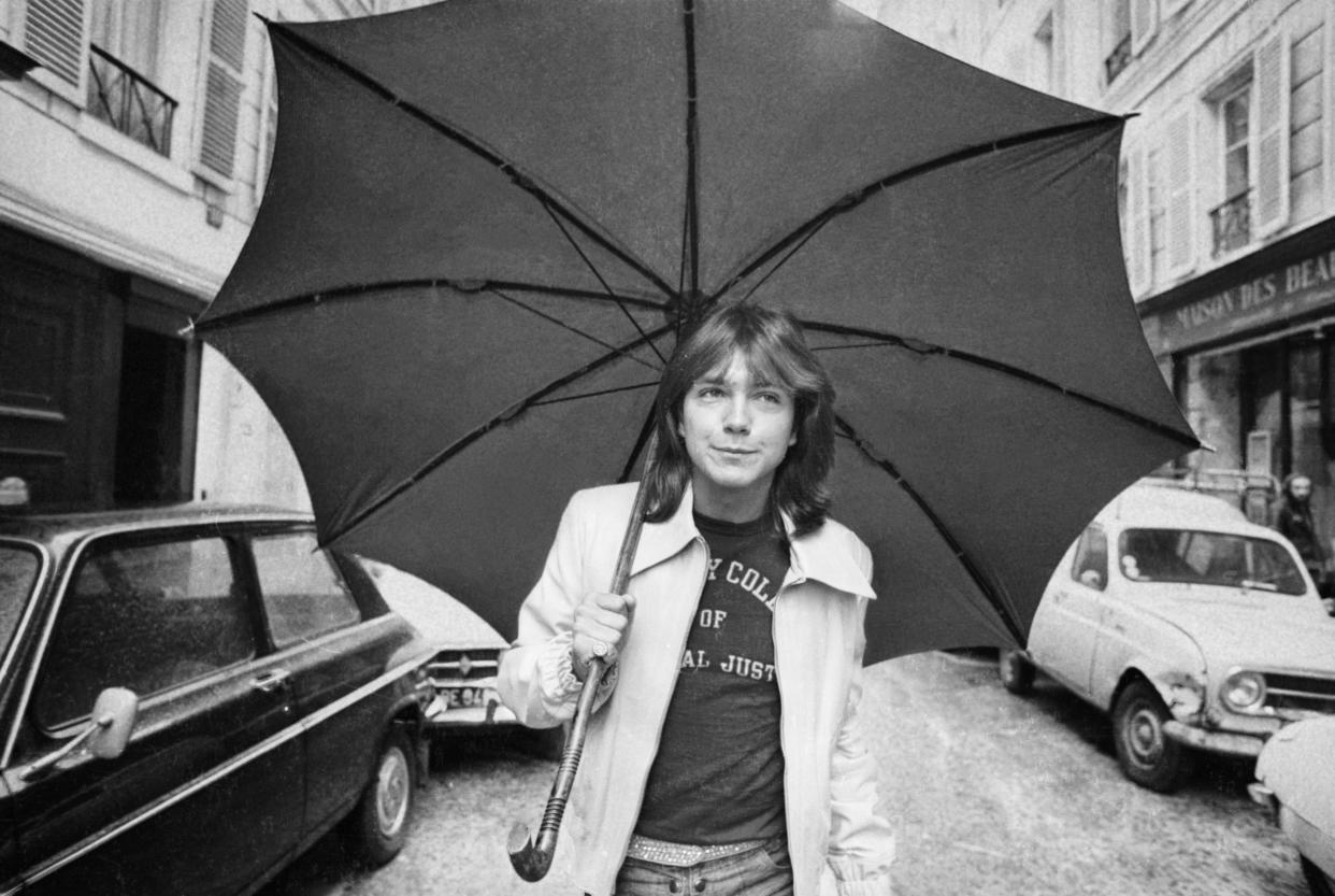 David Cassidy, American pop singer and star of the television programme 'The Partridge Family', walking down a road in Paris with an umbrella, 30th April 1974.