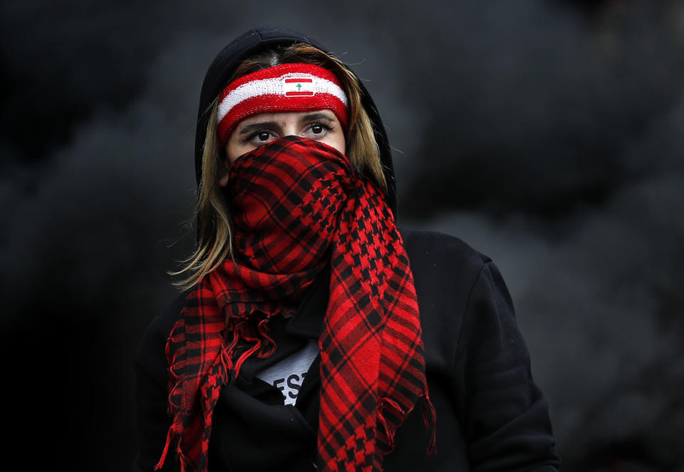 A protester covers her face by a scarf, as she blocks a main highway, during a protest in the town of Zouk Mosbeh, north of Beirut, Lebanon, Monday, March 8, 2021. The dayslong protests intensified Monday amid a crash in the local currency, increase of consumer goods prices and political bickering between rival groups that has delayed the formation of a new government. (AP Photo/Hussein Malla)