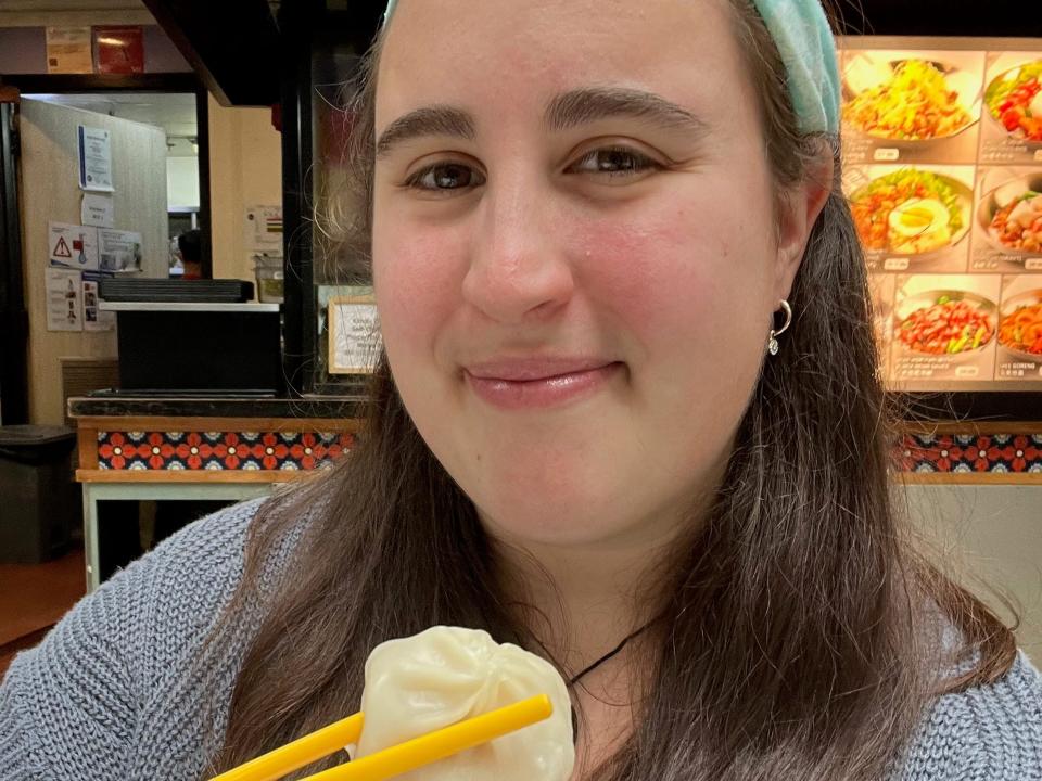 A selfie of the author with a soup dumpling in chopsticks.