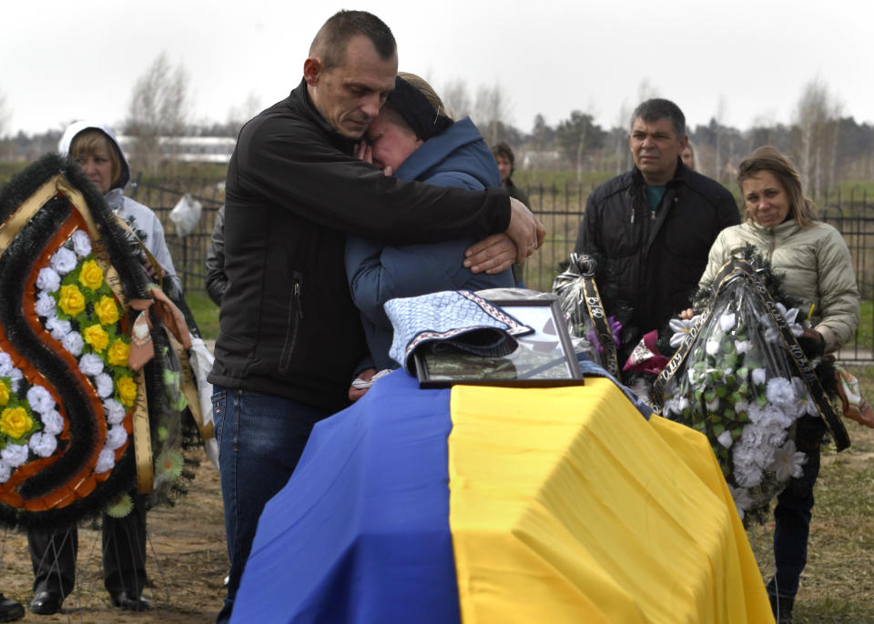 Two family members embrace near a coffin, draped in the colors of Ukraine, holding the remains of Bogdan Volodymerovuch Tromssa.