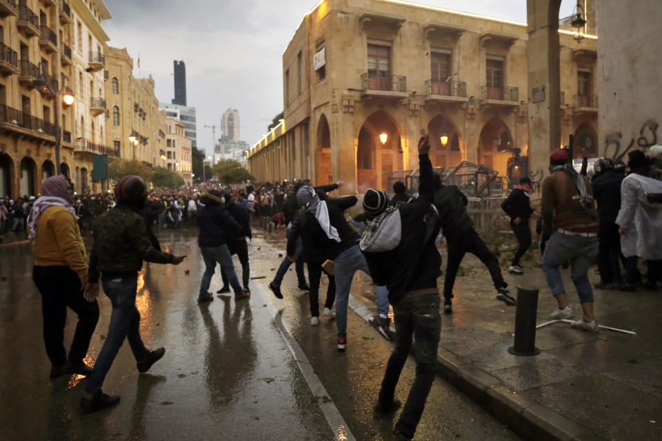 Anti-government demonstrators throw stones toward riot police at a road leading to the parliament building in Beirut, Lebanon, Saturday, Jan. 18, 2020. Riot police fired tears gas and sprayed protesters with water cannons near parliament building to disperse thousands of people after riots broke out during a march against the ruling elite amid a severe economic crisis. (AP Photo/Hassan Ammar)