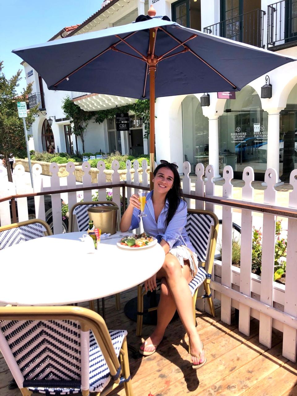 Anneta sits at a table holding a drink under an umbrella at the restaurant Jeannine's