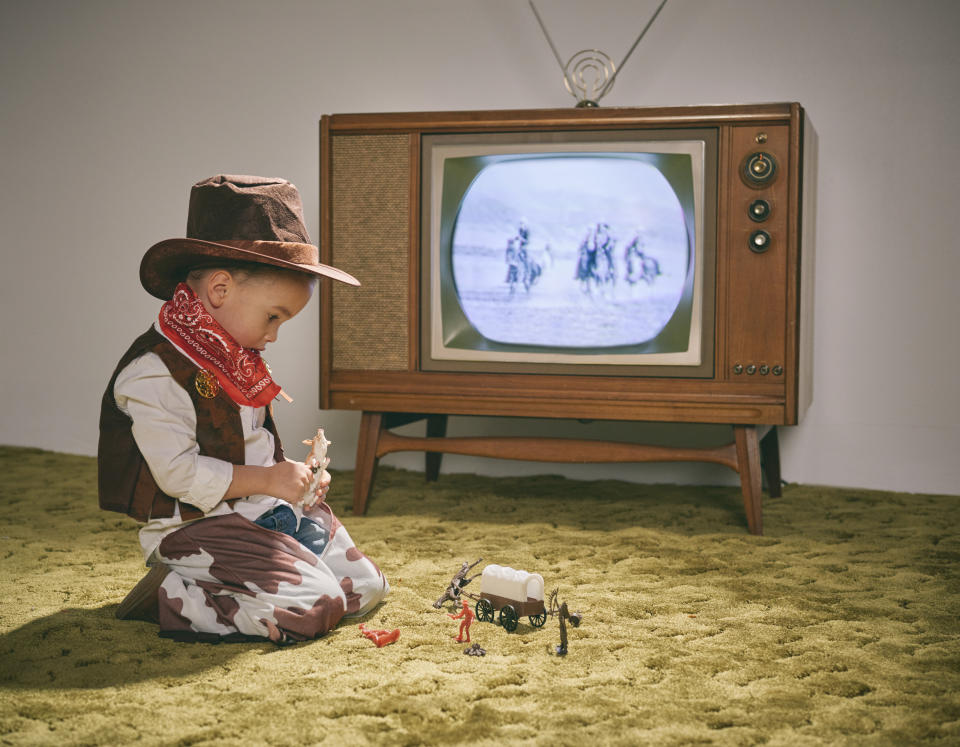 a little boy in a cowboy outfit watching westerns