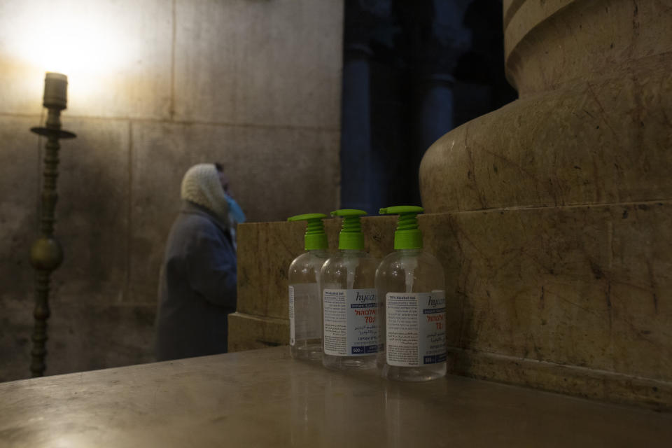 A woman attends mass next to three bottles of hand sanitizer available for worshippers at the Church of the Holy Sepulchre, where Jesus Christ is believed to be buried, during a third lockdown to curb the spread of the coronavirus, in the Old City of Jerusalem, Monday, Jan. 18, 2021. (AP Photo/Maya Alleruzzo)