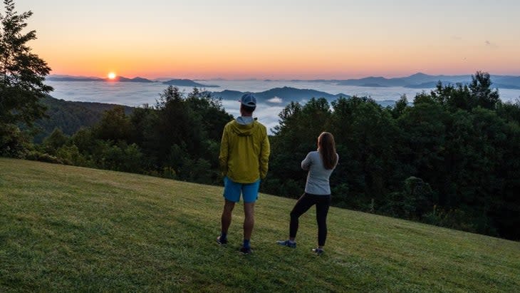 The author and his wife on the lawn of the Swag, looking down at the sunset and the horizon over the Smoky Mountains, with cloud cover in the lower valleys