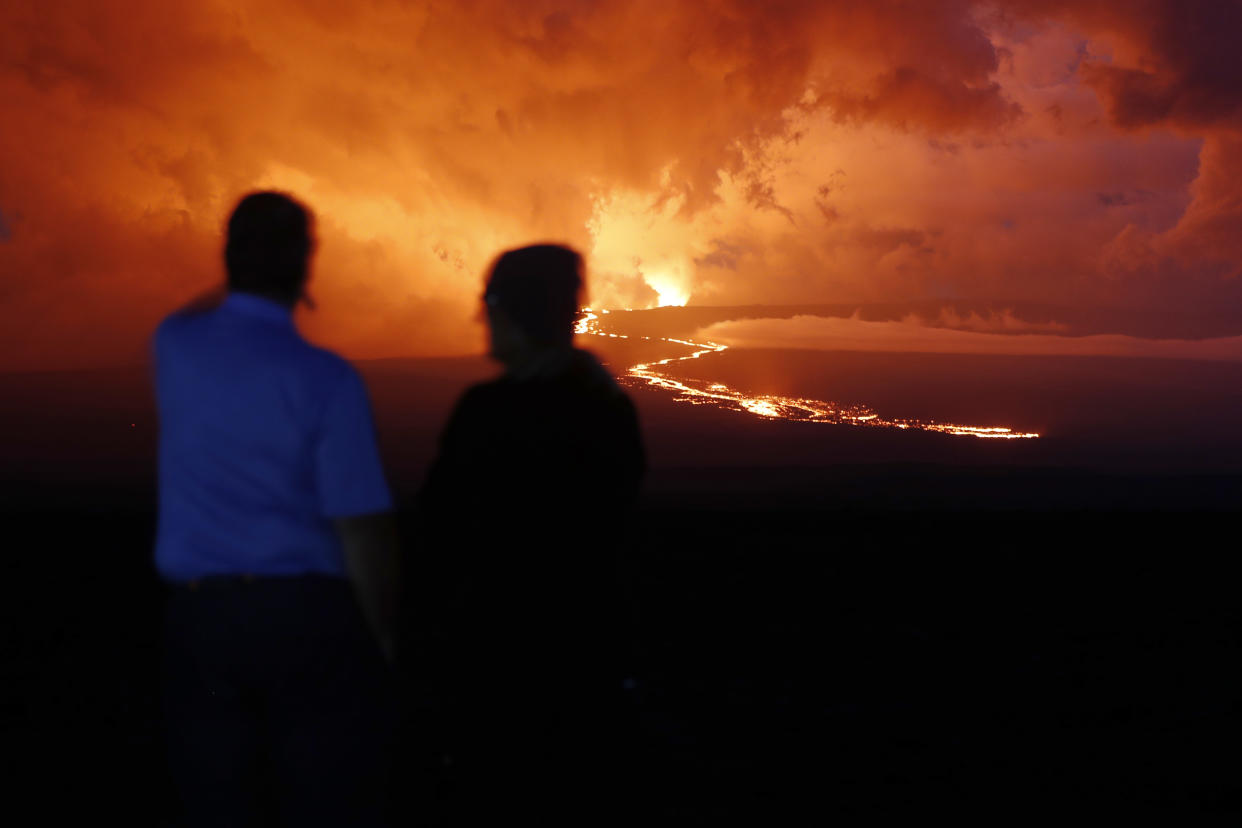 Spectators watch the lava flow down the mountain from the Mauna Loa eruption, Tuesday, Nov. 29, 2022, near Hilo, Hawaii. (AP Photo/Marco Garcia)